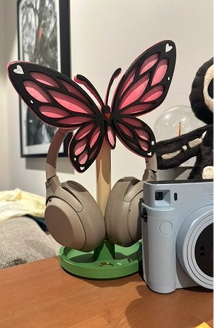 A paper butterfly ornament between a pair of headphones and an instant camera.
